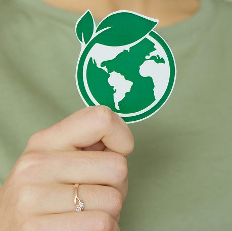 Gros plan d'une main tenant un autocollant vert représentant la Terre surmontée de deux feuilles, symbole d'écologie.