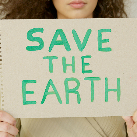 Gros plan d'une personne aux cheveux bouclés, dont on ne voit que le bas du visage et les mains, tenant un cahier de croquis en papier kraft recyclé à reliure spirale.